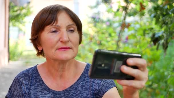 Портрет стильной пожилой женщины с черным смартфоном и селфи — стоковое видео