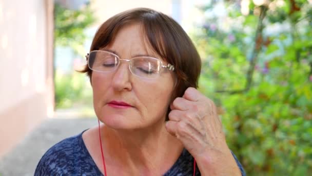 Літня жінка носить червоні навушники і слухає музику — стокове відео