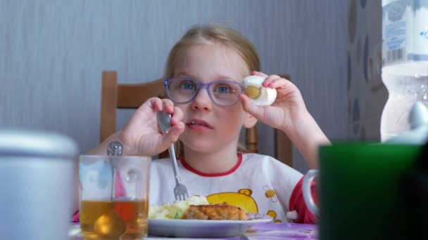 Pequena menina bonita comendo um ovo cozido na mesa na cozinha — Vídeo de Stock