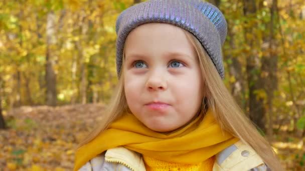 Roztomilá holčička je jablko a usmívá se v parku na podzim — Stock video