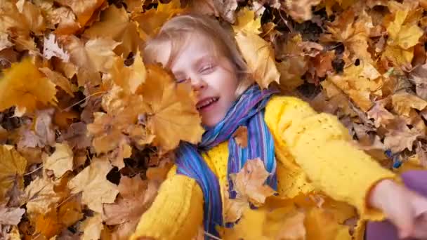 Souriant heureuse petite fille couchée sur les feuilles d'automne — Video