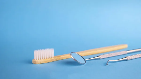 牙科诊所的牙医工具 牙医镜和钩子 白色木制牙刷 口腔卫生与健康概念图 蓝色背景 文本的复制空间 — 图库照片