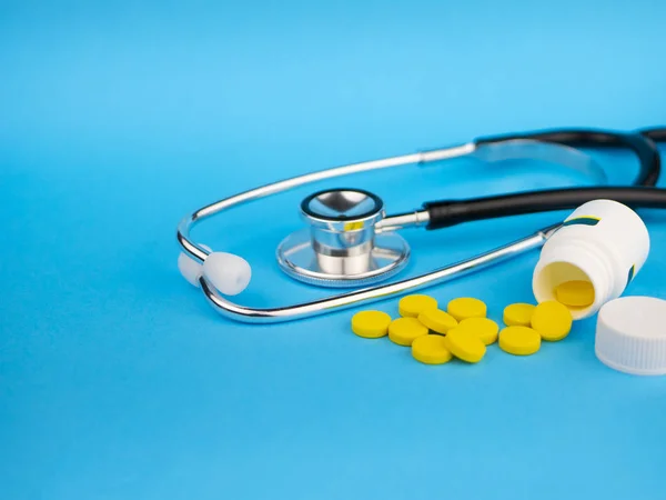 Black stethoscope for doctor and yellow pills and plastic white bottle. Healthcare concept. Blue background with copy space for text