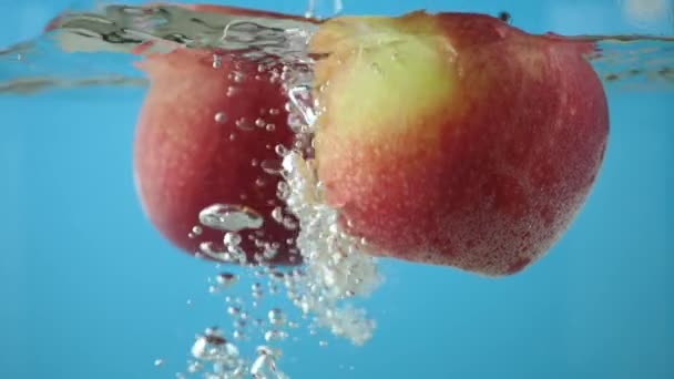 青色の背景色に透明な泡の道で水の下で赤い黄色いリンゴ スローモーション水しぶき概念 スローモーション水しぶきコンセプト — ストック動画