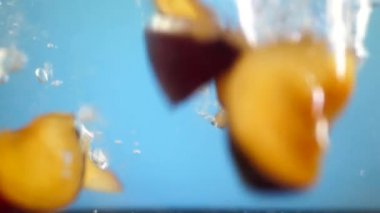 Olgun erik ile mavi arka plan, hava kabarcıkları suyun altına düşen dilimler. Yavaş hareket su sıçramasına veya sağlıklı vejetaryen gıda beslenme kavramı