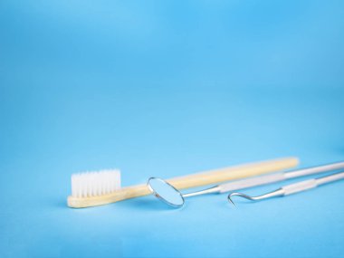 Diş hekimi diş office araçlarında: diş hekimi ayna ve kanca, beyaz tahta diş fırçası. Dişlerle ilgili sağlık bilgisi ve sağlık kavramsal görüntü. Metin için kopya yer ile mavi arka plan