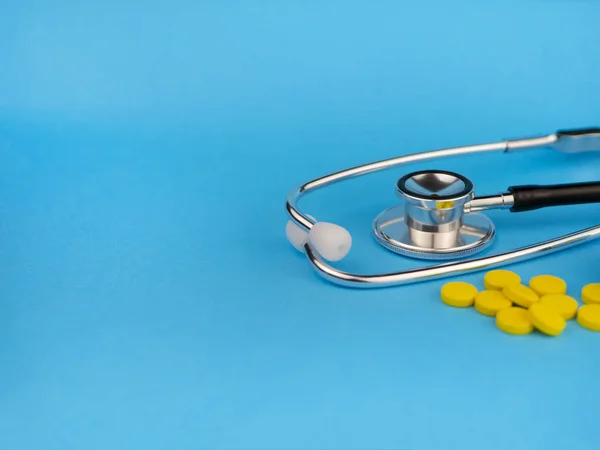 Black stethoscope for doctor and yellow pills. Healthcare concept. Blue background with copy space for text