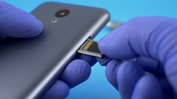 Trabajador técnico en guantes azules instala tarjeta micro SD en teléfono celular gris — Vídeo de stock