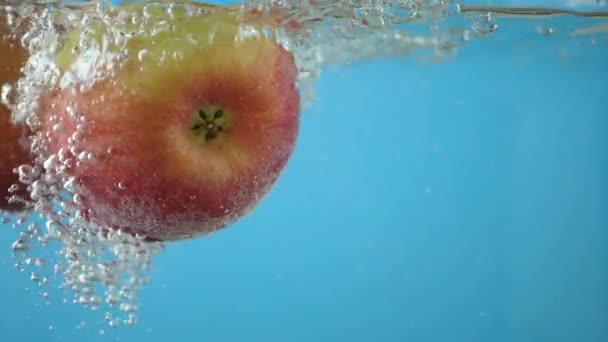 Красное желтое яблоко под водой со следом прозрачных пузырей — стоковое видео