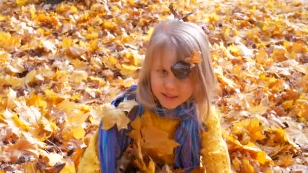 Little cute girl throwing up leaves at park in autumn — Stock Video