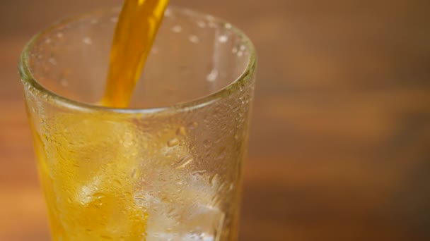 Оранжевый лимонад наливают в холодное стекло с кубиком льда — стоковое видео