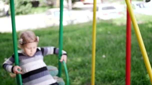Malá holčička jede po houpačkách na hřišti — Stock video