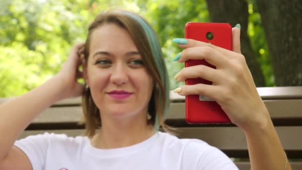 Krásná žena úsměvy a dělat selfie v parku — Stock video