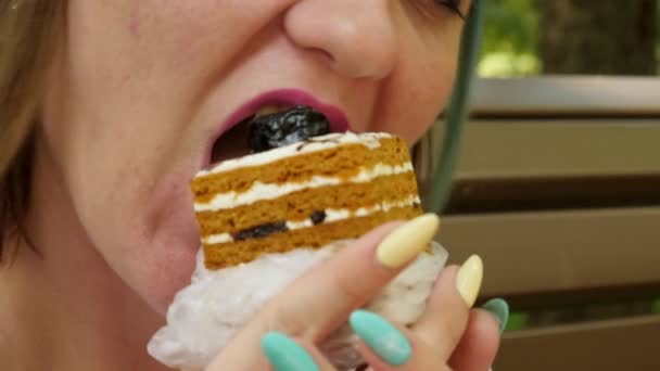 Manger un gâteau féminin est assis sur un banc brun dans le parc — Video