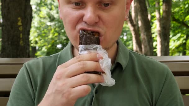 Macho comiendo pastel de chocolate en el parque — Vídeo de stock