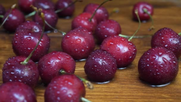 Čerstvé třešně s kapkami vody na hnědé dřevěné pozadí — Stock video