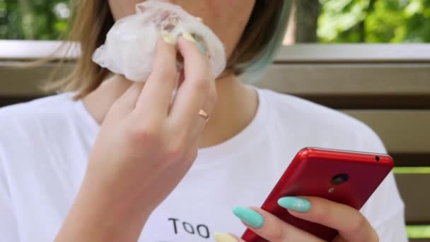 Чарівна молода жінка читає повідомлення на смартфоні і їсть торт — стокове відео