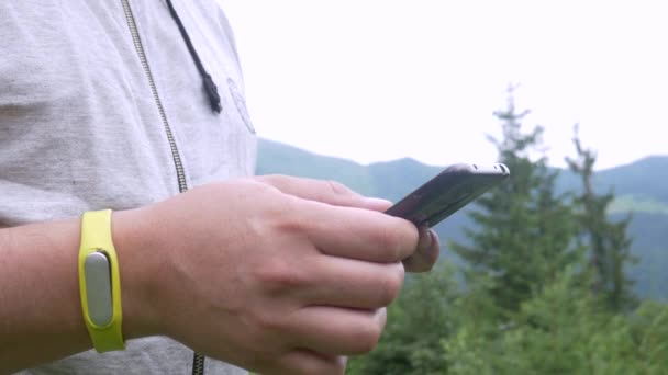 Nerozeznatelné mužské ruce používající smartphone na pozadí horského lesa — Stock video