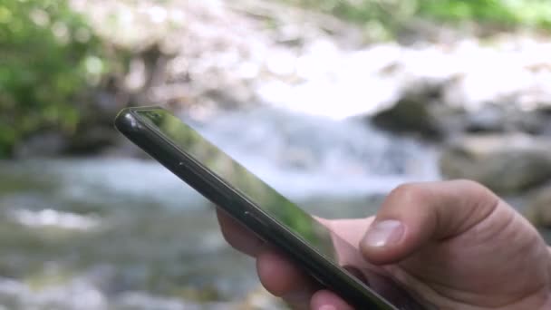 Wandelaar mannelijke handen met behulp van Smartphone op Mountain Stream achtergrond — Stockvideo