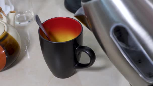 Verter agua hirviendo de la tetera eléctrica en una taza de cerámica negra amarilla roja — Vídeos de Stock