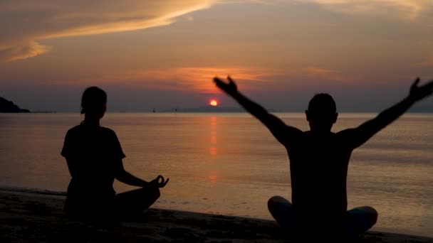 Erkek ve kadın, turuncu bulutlu arka planda deniz suyu yüzeyinde yoga yapıyorlar. — Stok video