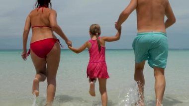 Kız, baba ve anne kumsalda koşuyor.
