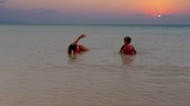 Anne ve kızı dramatik güneş batarken deniz suyu yüzeyinde uzanırlar.