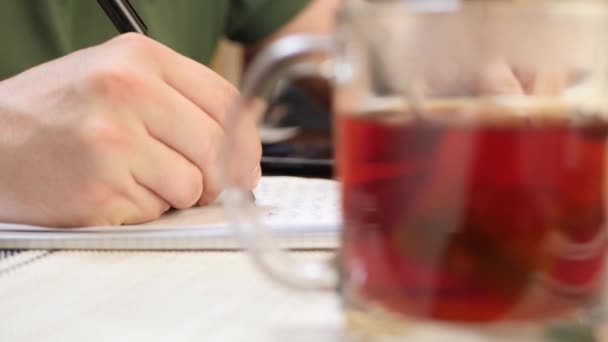 Schrijft informatie in papieren notitieboekje, leest boek, drinkt warme thee, voor te bereiden op examen — Stockvideo