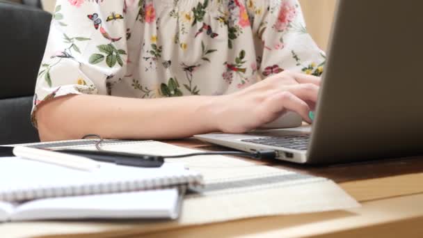 女性はノートパソコンのキーボードに情報を入力し、ノートブックにペンでテキストを書きます — ストック動画