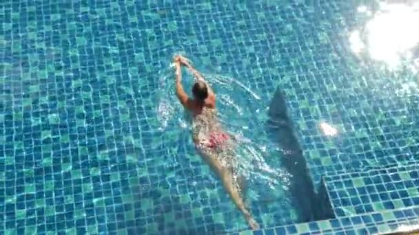 Elegance female in red swimsuit swim in swimming pool in sunlights on resort backyard — Stock Video