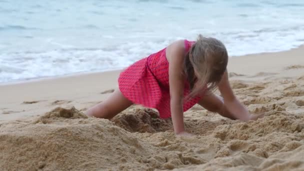 Девочка роет и играет в песок на берегу моря — стоковое видео