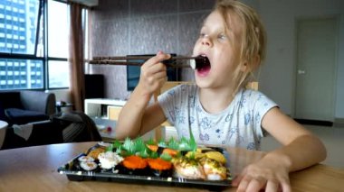 Küçük kız yemek çubuğuyla suşi yiyor.