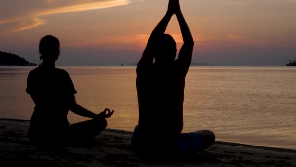 Man and womans silhouette sits in lotus position, meditating and does yoga excercises on sunset — Stock Video