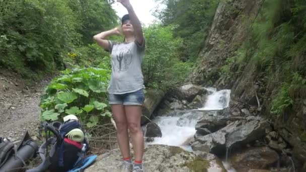 Жінка мандрівник фотографує блог стоячи біля потоку в горах — стокове відео