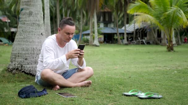 Красивий студент-чоловік використовує смартфон біля пальми — стокове відео