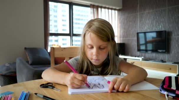 Linda niña sentada en la mesa de madera en la habitación y dibujo cuadro con marcadores de colores en el libro de bocetos — Vídeo de stock