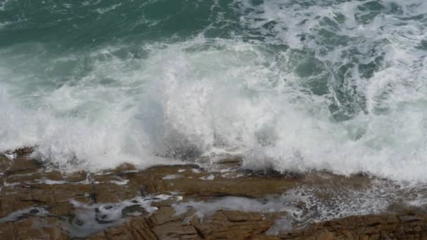 Волны брызгают на скалы в солнечный ветреный день — стоковое видео