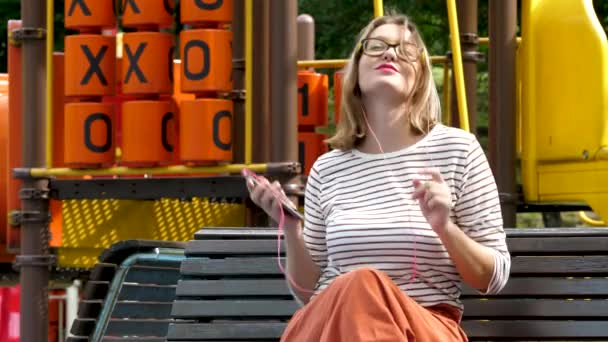 Jonge mooie vrouw luistert naar muziek door hoofdtelefoon en smartphone — Stockvideo