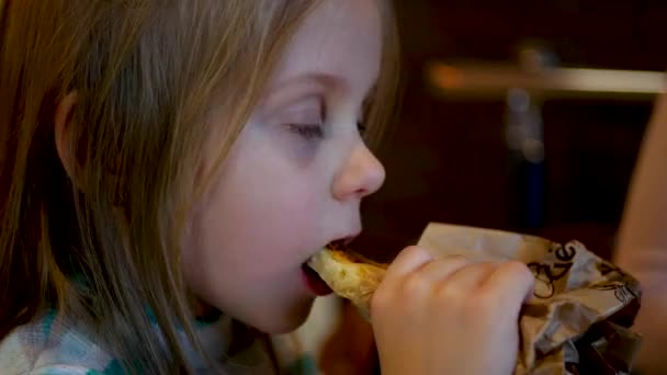 Kleines Mädchen isst auf verschwommenem Einkaufszentrum-Hintergrund — Stockvideo