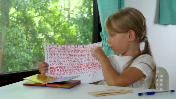 어린 소녀는 집의 푸른 나무 배경에서 숙제를 한다 — 비디오