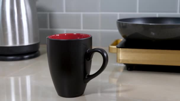 Café instantáneo granulado concentrado verter en taza de cerámica negra en la mesa de la cocina — Vídeos de Stock