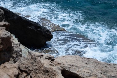 Büyük turkuaz dalgalar kayalıklara çarpıyor. Açık mavi gökyüzünün altında, arka planda yalnız dağlar yükselir. Hiç kimse, seyahat, macera, turizm, doğa, kıyı keşfi ve Akdeniz manzara fotoğrafçılığı için mükemmel..
