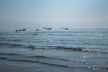 Güzel bir sabah deniz manzarası, boş bir rıhtım, sakin mavi bir su, ve uzakta yatlar. Yumuşak dalgalar bulutlu parlak bir gökyüzünün altındaki kumlu sahile dokunur, sakin bir sahil tatil atmosferini yakalar..