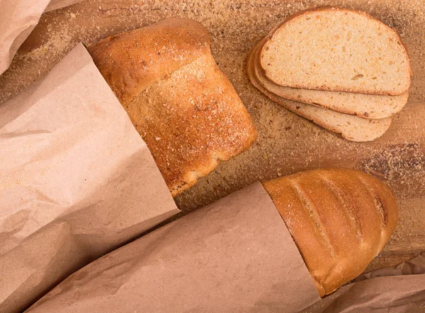 Fresh bread and loaf packaging in kraft paper on a wooden board