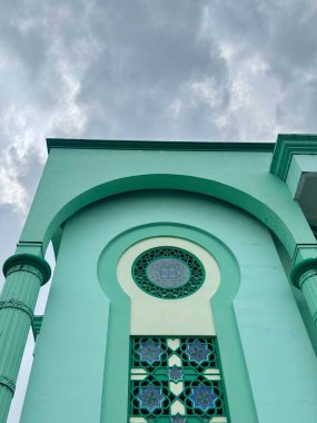 Zarif nane yeşili cami cephesi, süslü geometrik pencereli dramatik bulutlu gökyüzüne karşı