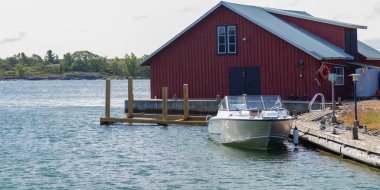 Small boat on the pier near traditional sheds in a Finnish fishing village by the Baltic Sea. Peaceful coastal life, Nordic heritage, and maritime culture