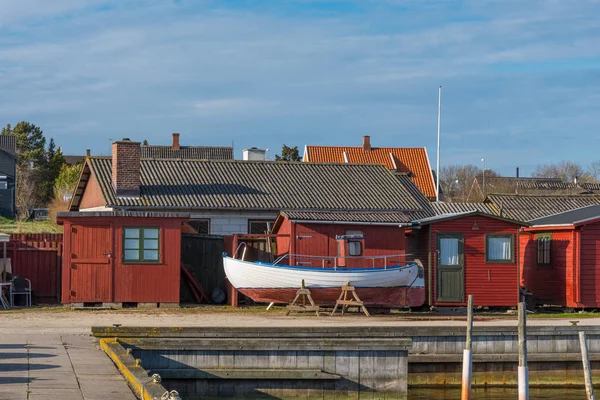 Old fishing boat in front of red sheds — Stock Photo, Image