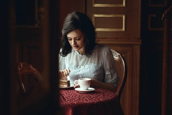 Fiatal gyönyörű lány ül az asztalnál a szép kávézóban, és levágta egy darab finom csokoládétorta — Stock Fotó