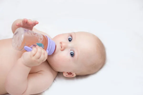 a portrait of an infant drinking juice from a bottle and lying