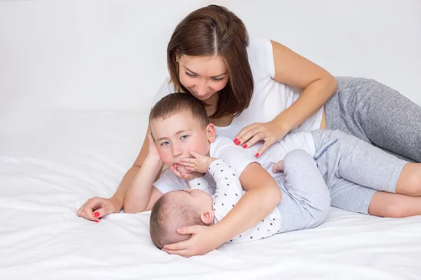 Young mom with her 5 year old son and 4 months old baby playing on a bed